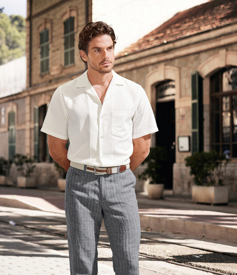 Ceinture italienne en lin et cuir Homme en chemise Panama blanche avec un pantalon rayé gris dans la rue.