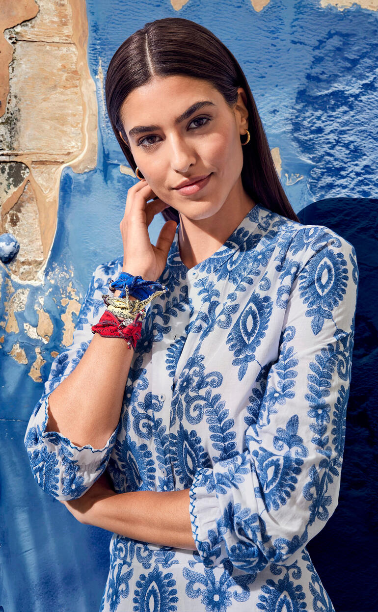 Gros plan d'une femme en robe à motifs bleus, souriant à la caméra.