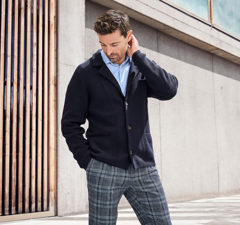 Homme en blazer en tricot côtelé Pima regardant pensivement ses vêtements.