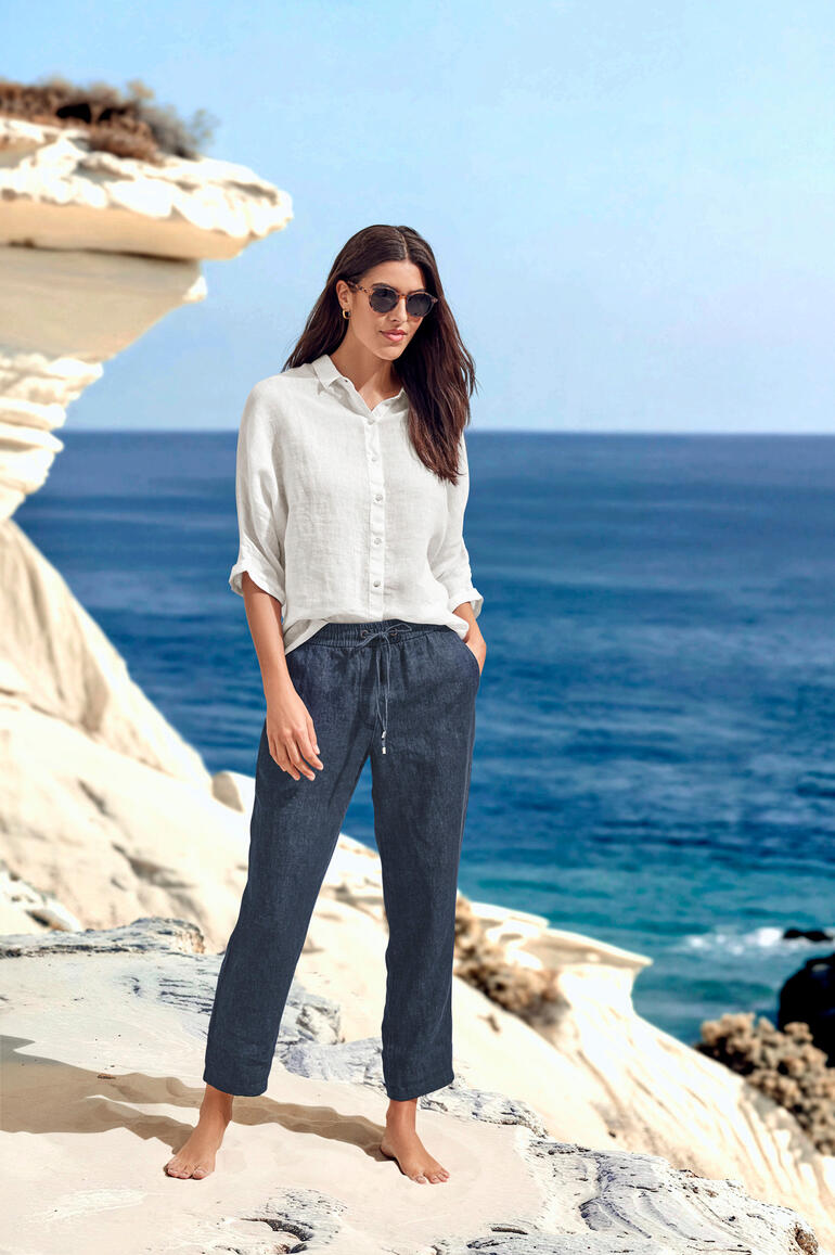 Femme en blouse légère et pantalon au bord de la mer.
