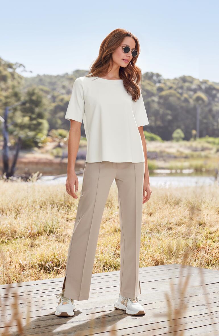 Sneaker glamour Alexander Smith Femme en chemisier blanc et pantalon beige dans un jardin d'automne.