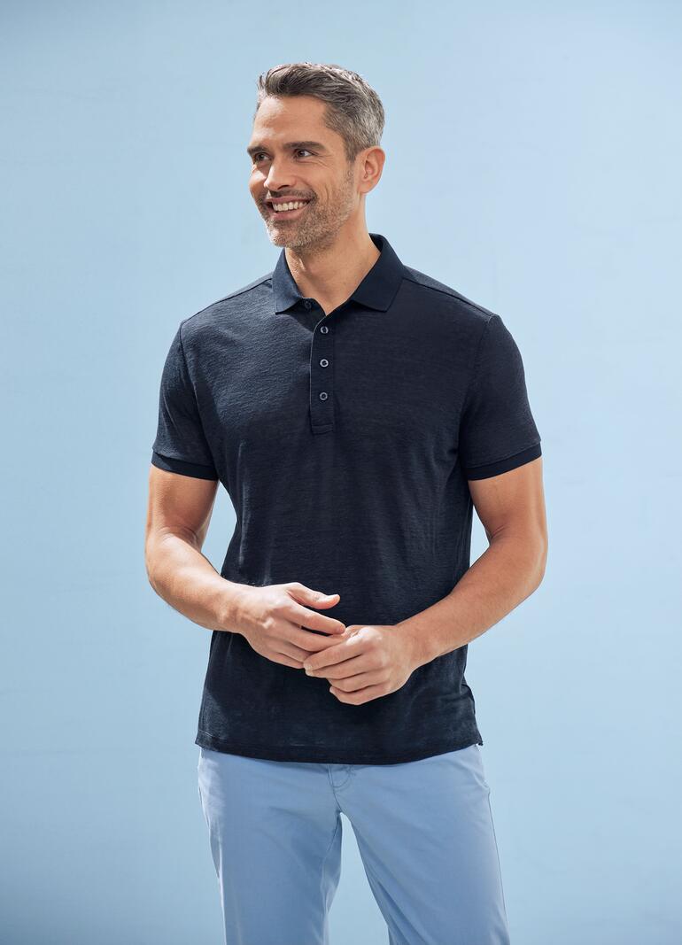 Homme habillé en noir avec un polo bleu foncé sur fond bleu.