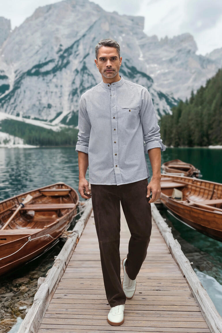Pantalon 5 poches en suède de chèvre OCONI Homme en chemise rayée marchant le long d'un pont en bois près de bateaux au bord du lac.