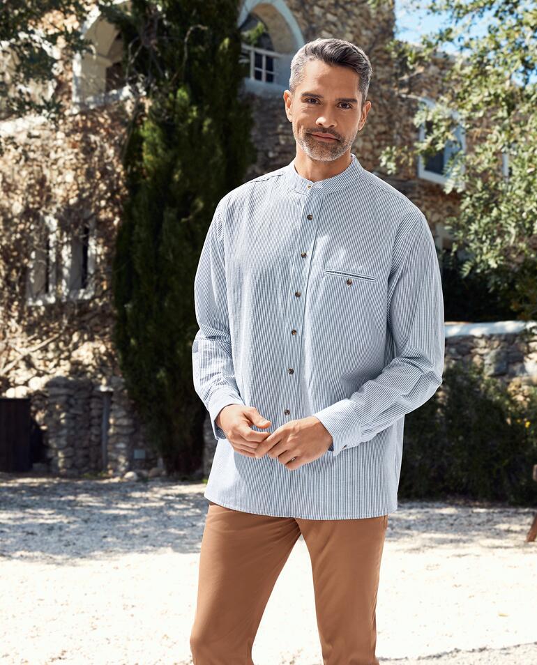 Homme souriant portant une chemise Grandfather rayée devant un fond en pierres.