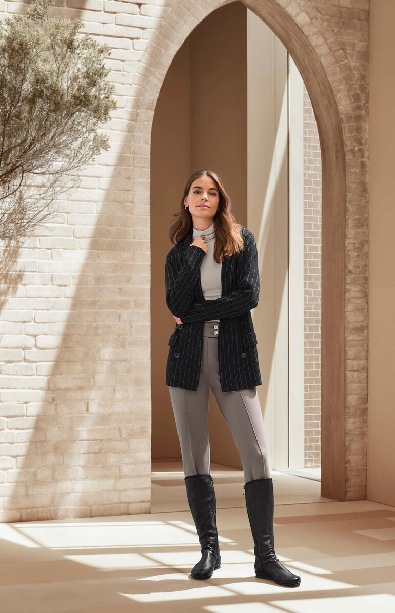 Noir Femme en pantalon de bottes et veste dans une pièce lumineuse.