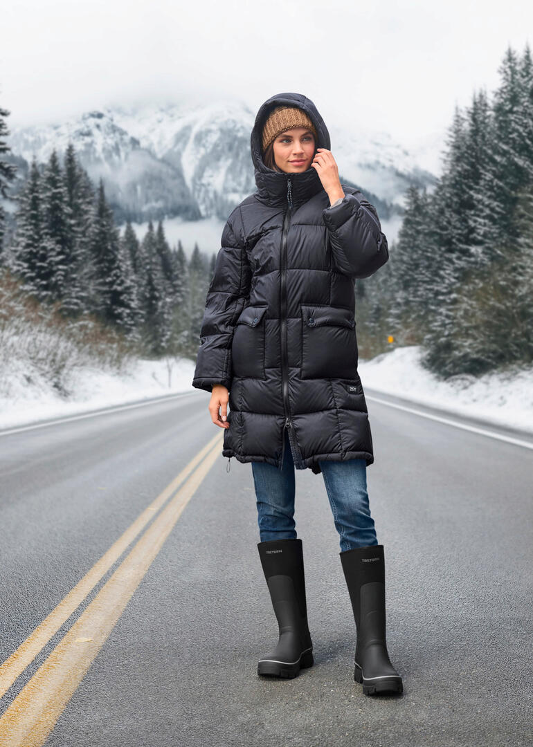 Bottes en caoutchouc hivernales Tretorn Femme en parka en duvet Taion avec capuche debout dans un paysage d'hiver.