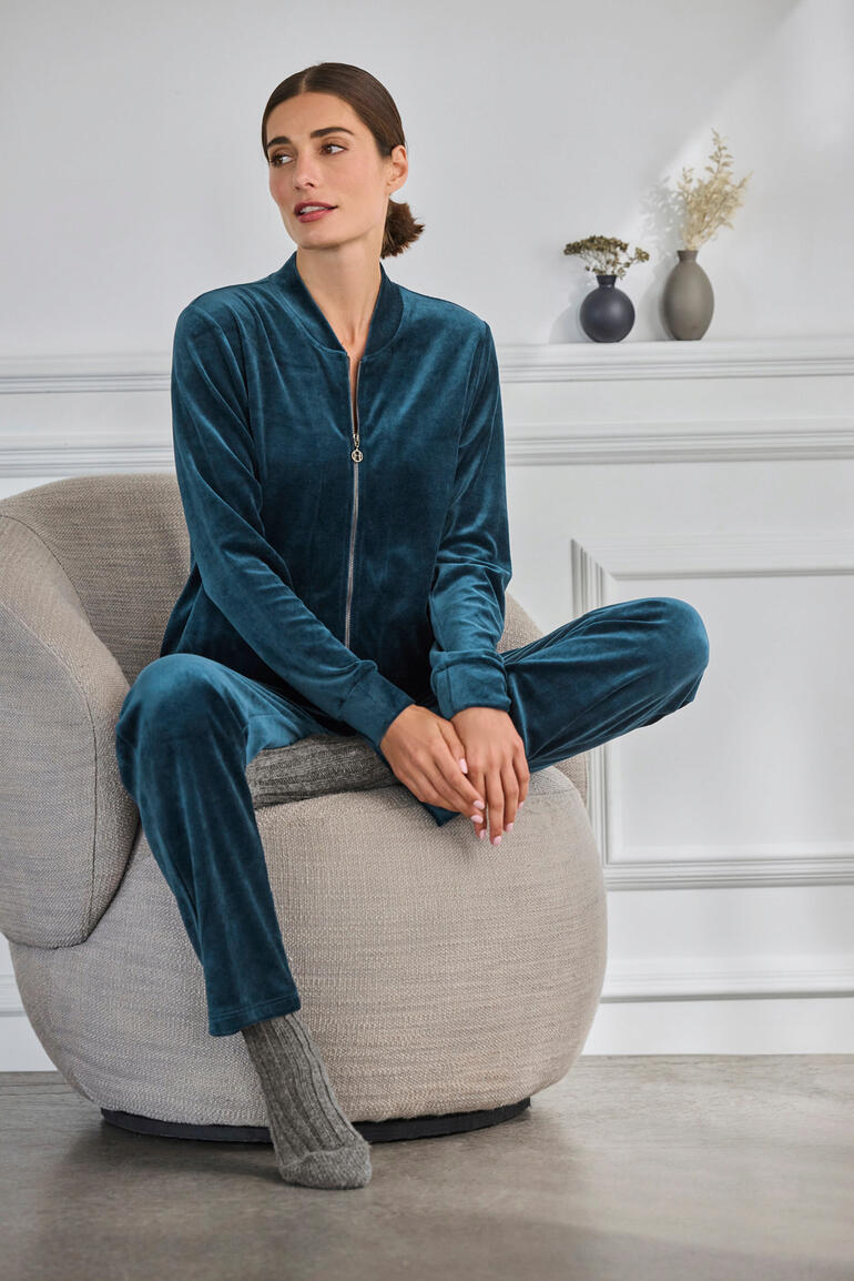 Femme assise dans un fauteuil confortable, portant un ensemble en velours Hanro vert.
