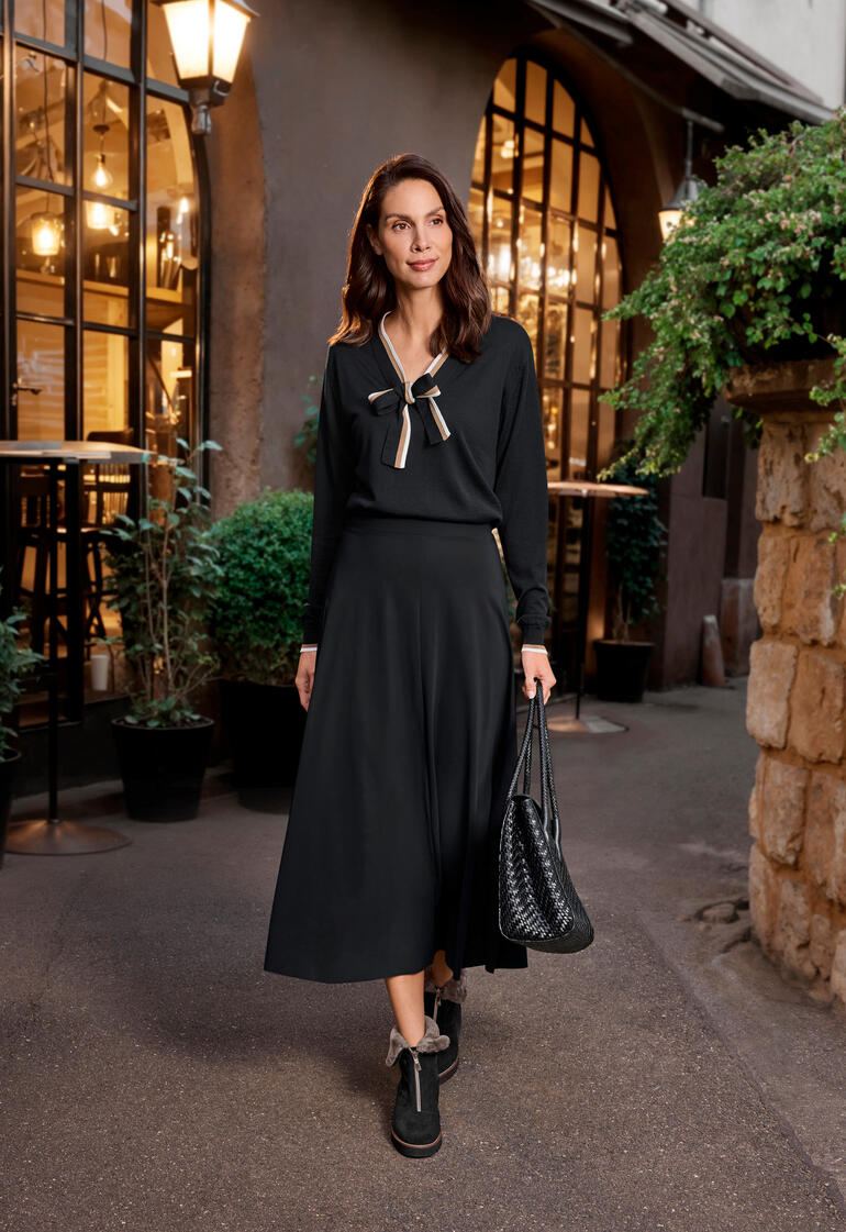 Femme en robe noire avec nœud sur le trottoir devant un café