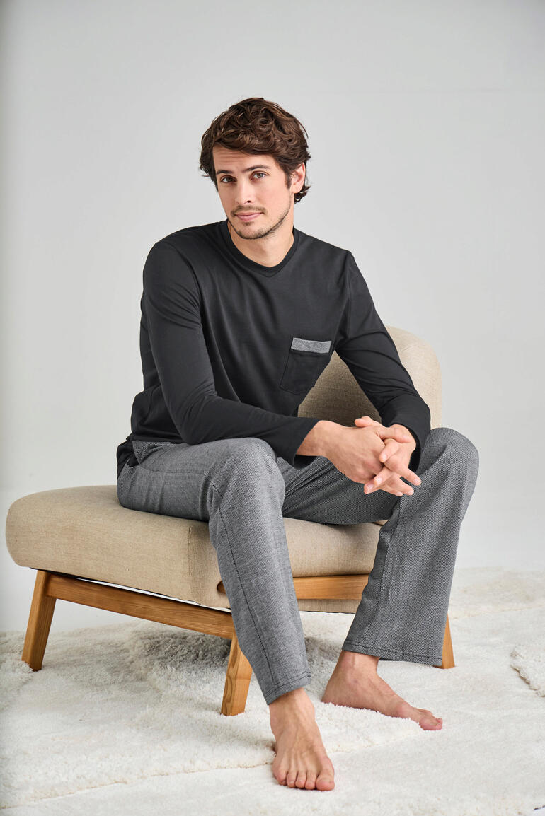 Homme assis sur une chaise en t-shirt noir à manches longues et pantalon de pyjama gris.