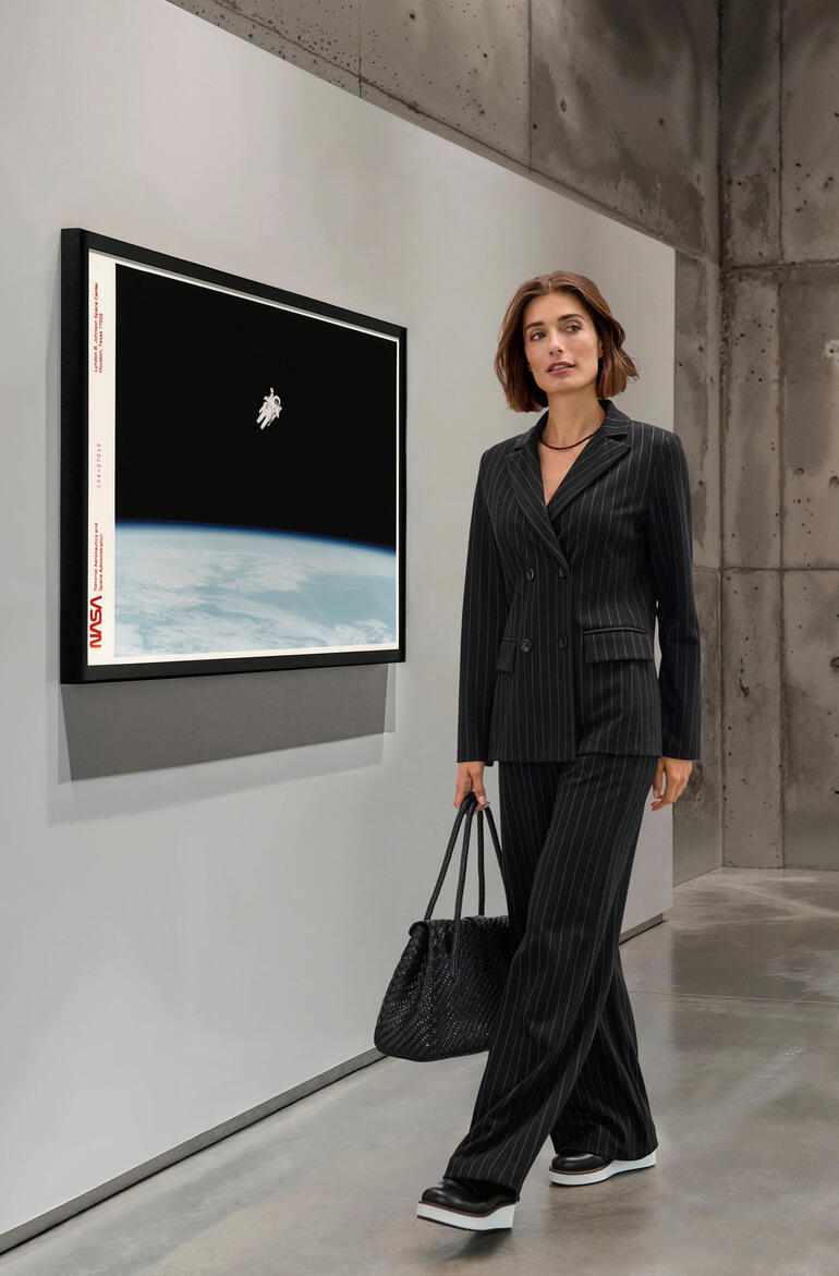 Femme en costume à rayures devant une œuvre d'art dans un espace moderne.