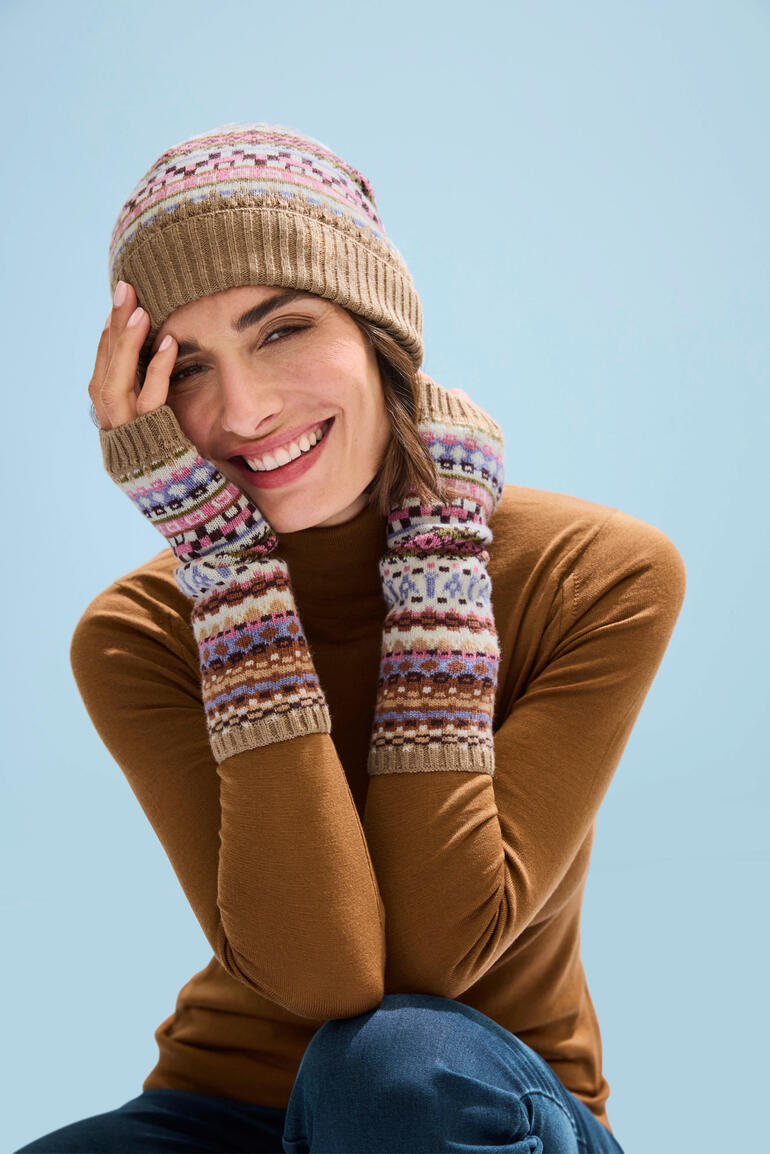 Bonnets et Manchettes Femme portant un bonnet jacquard et des mitaines, souriante dans un environnement hivernal.