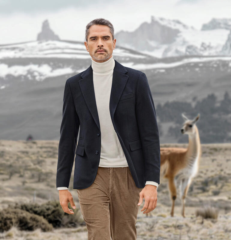 Blazer en vicuña bleu marine, modèle marchant à travers le paysage avec un lama en arrière-plan.