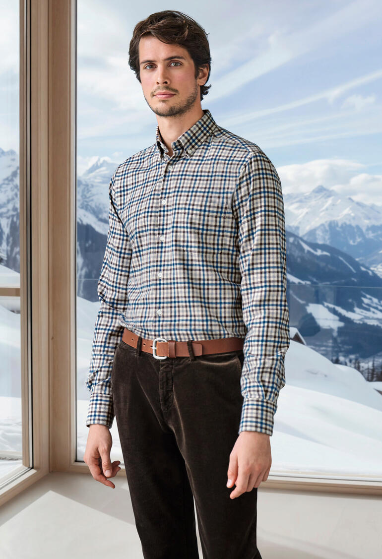 Homme en chemise en flanelle de laine à carreaux devant un paysage montagneux.