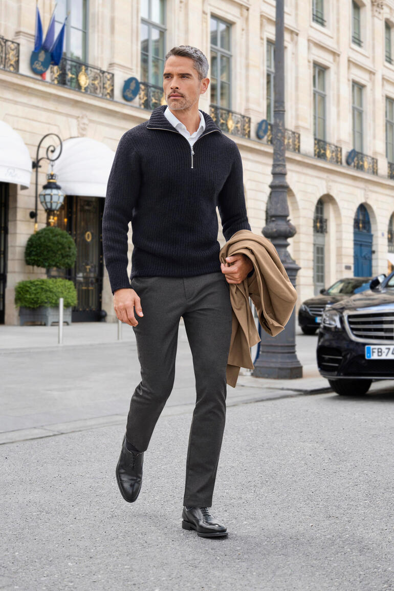 Homme portant un pull possum noir, marchant élégamment dans la rue.