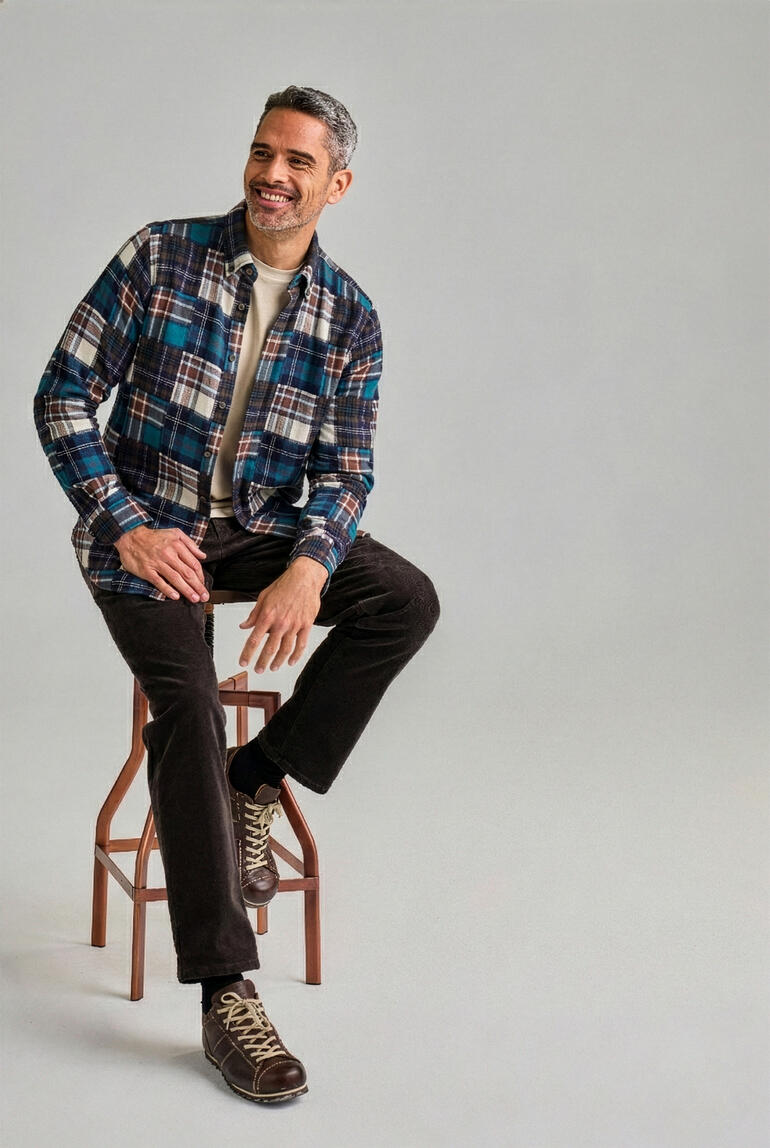 Homme assis sur un tabouret, portant une chemise en flanelle à carreaux bleus et bruns.