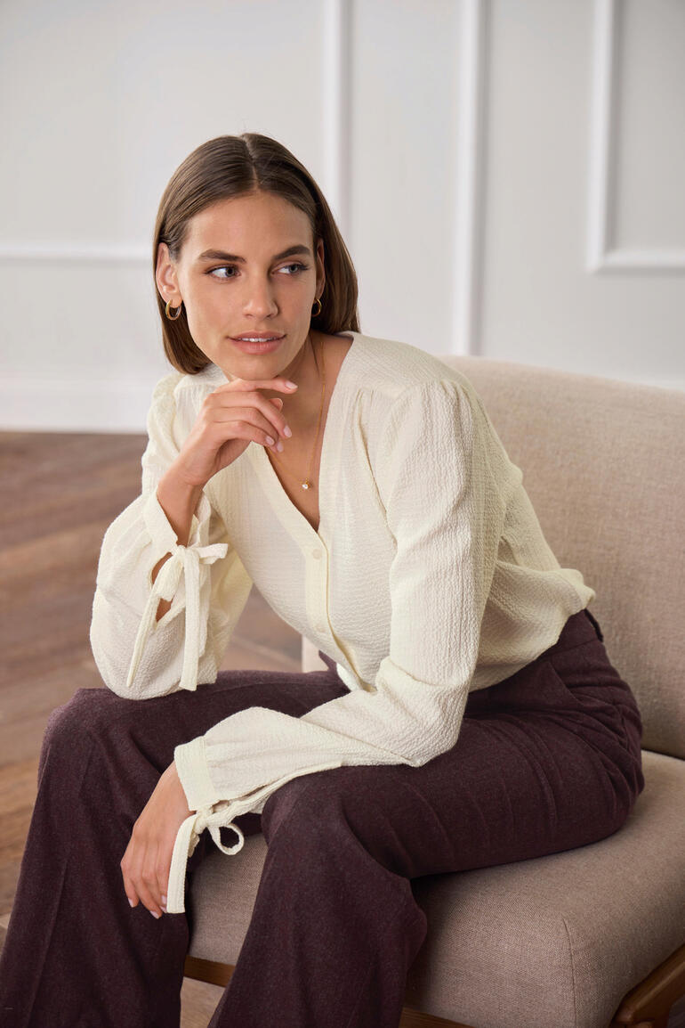 Femme assise dans une blouse en coton-cachemire claire avec des manches nouées.