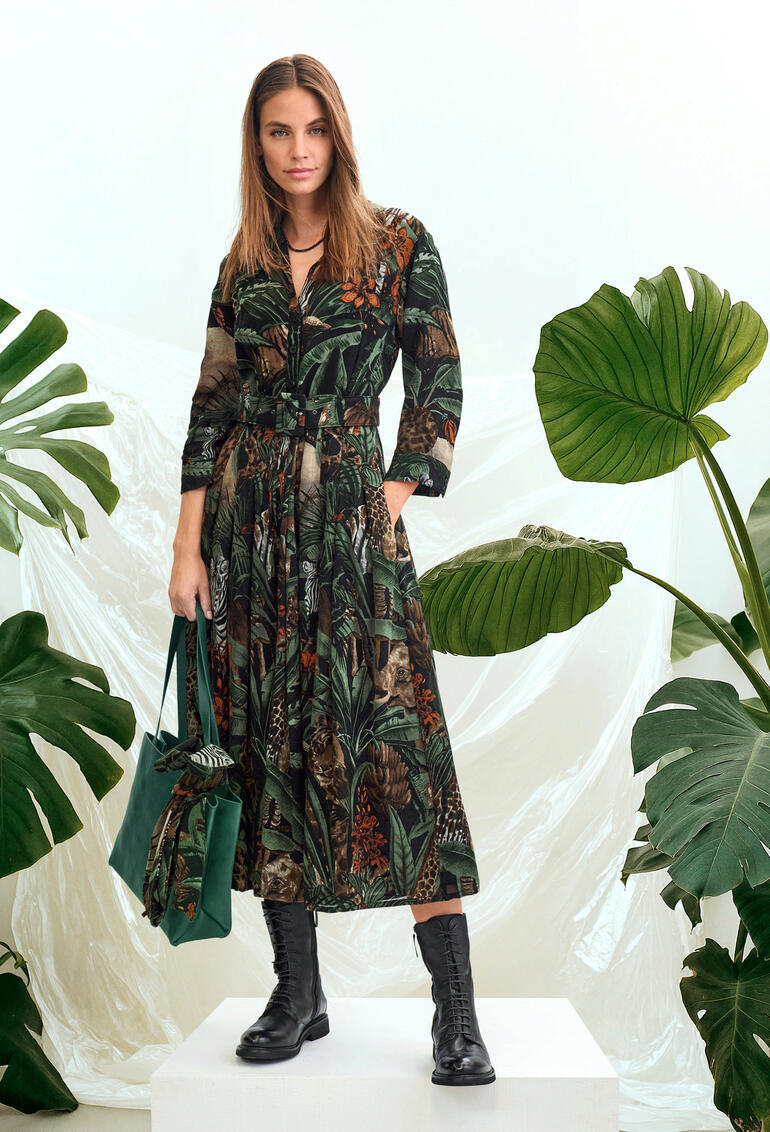 Robe en laine Jungle Samantha Sung Femme dans une robe en laine longue avec un motif jungle, devant des plantes tropicales.