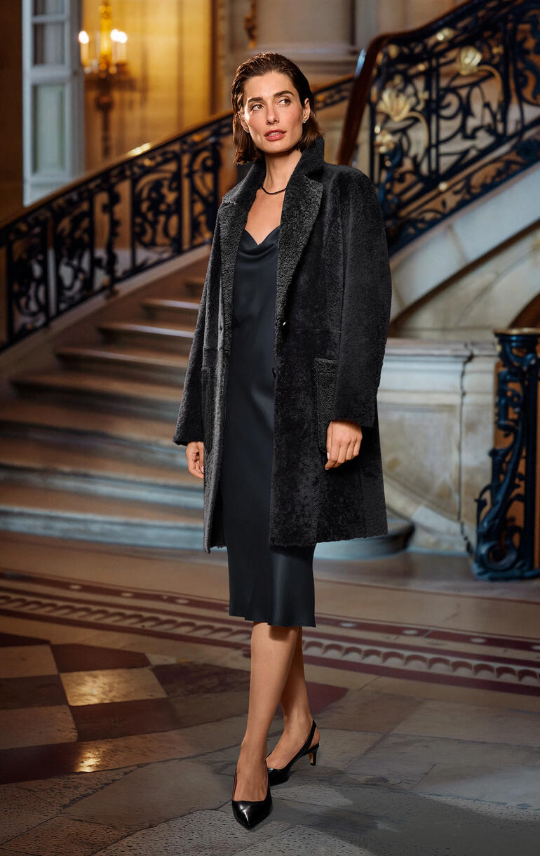 Manteau réversible en cuir d’agneau Arma Femme dans un manteau réversible en peau de mouton, posant dans un intérieur élégant.