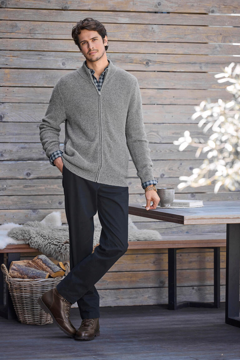 Homme en cardigan en alpaga gris devant un mur en bois