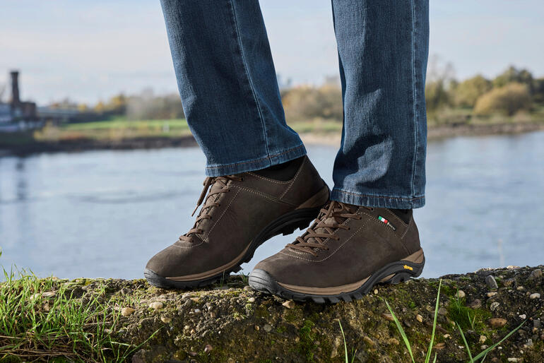Baskets brunes Zamberlan Commute GTX sur un rocher près d'un plan d'eau.
