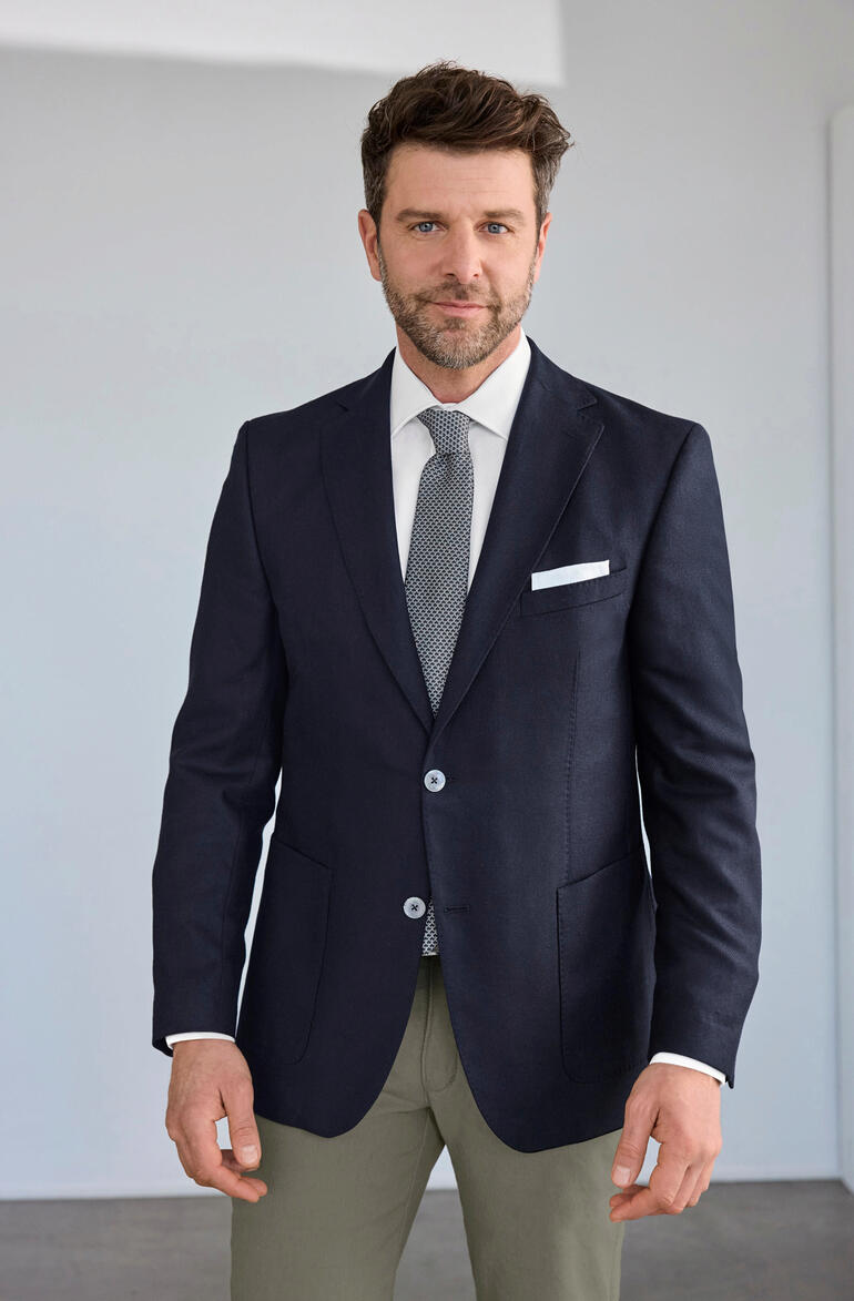 Veste en soie Carl Gross Homme en veste en soie Carl Gross avec cravate, posé devant un fond neutre.