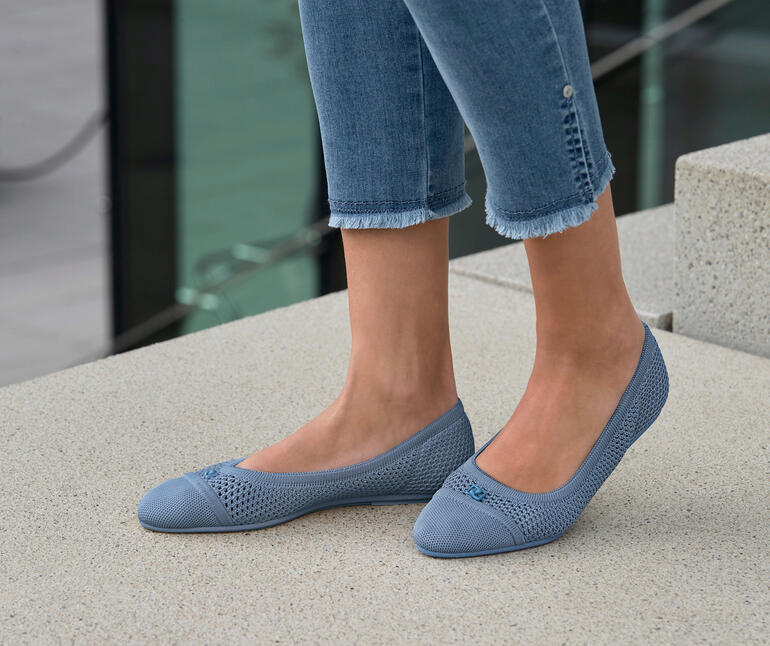 Bleu Femme portant des ballerines en mesh bleues, debout à l'extérieur sur un sol en pierre.
