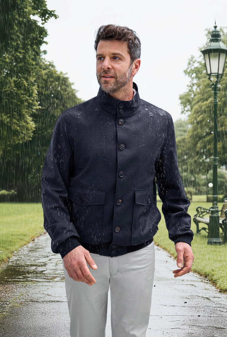 Gros plan d'un homme portant un blouson Storm-System® qui absorbe la pluie sur un fond bleu.