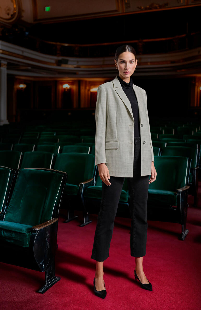 Blazer en bébé alpaga Clark Ross Femme en haut noir côtelé et blazer gris se tenant dans un théâtre.