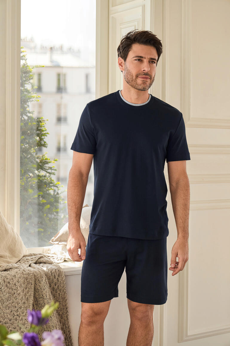 Homme debout dans une pièce lumineuse portant un pyjama de récupération bleu marine avec un short.