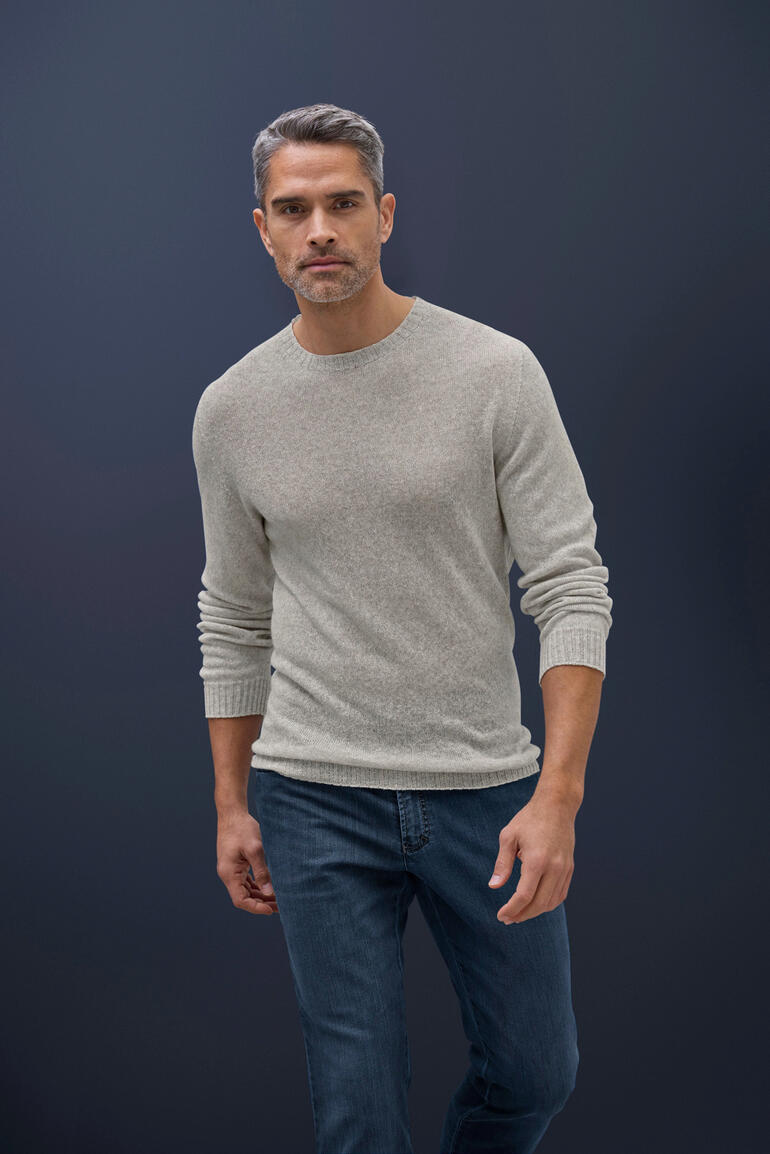 Taupe Homme portant un pull en cachemire-lin gris clair et un jean devant un fond sombre.