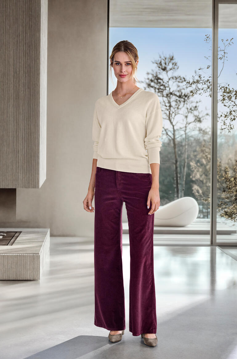 Femme portant un pantalon large en velours côtelé bordeaux et un pull en V
