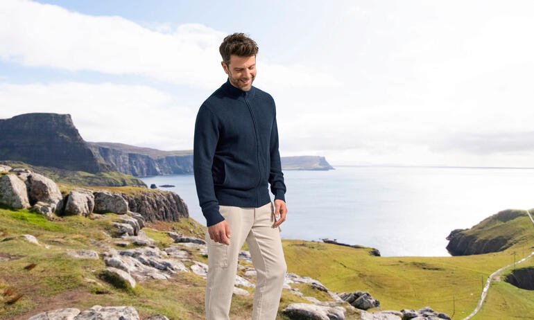 Homme portant un cardigan en soie Klima bleu marine, se tenant devant un paysage côtier.