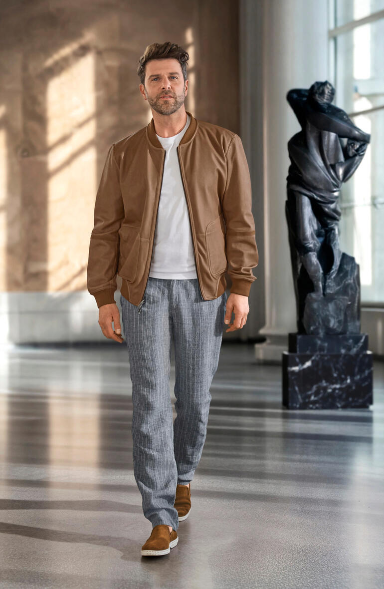Blouson réversible métis OCONI Homme portant une veste réversible OCONI Metis marron, avec une statue en arrière-plan.