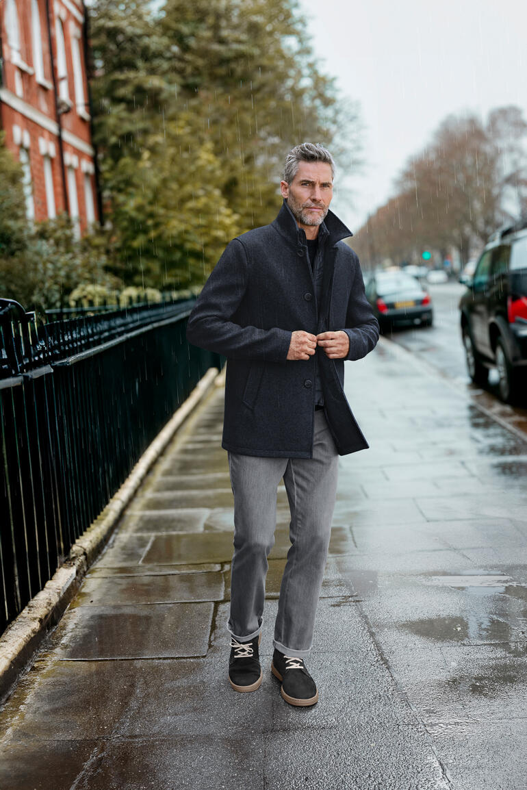 Manteau en laine respirant Geox en gris foncé, porté par un homme sur une rue humide.