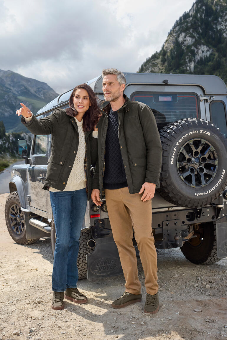 Couple en vestes d'extérieur se tient devant un véhicule tout-terrain dans un environnement naturel.