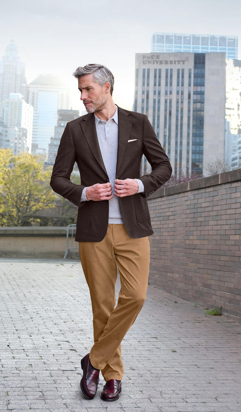 Homme en blazer marron se tient dans un environnement urbain.