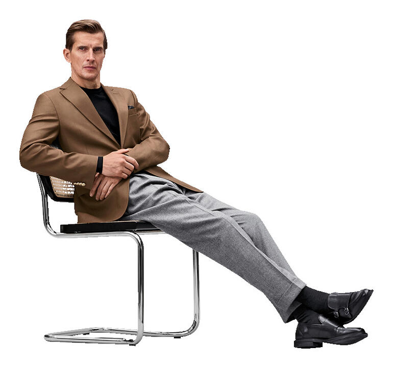 Homme assis dans un blazer marron sur une chaise avec une posture décontractée.