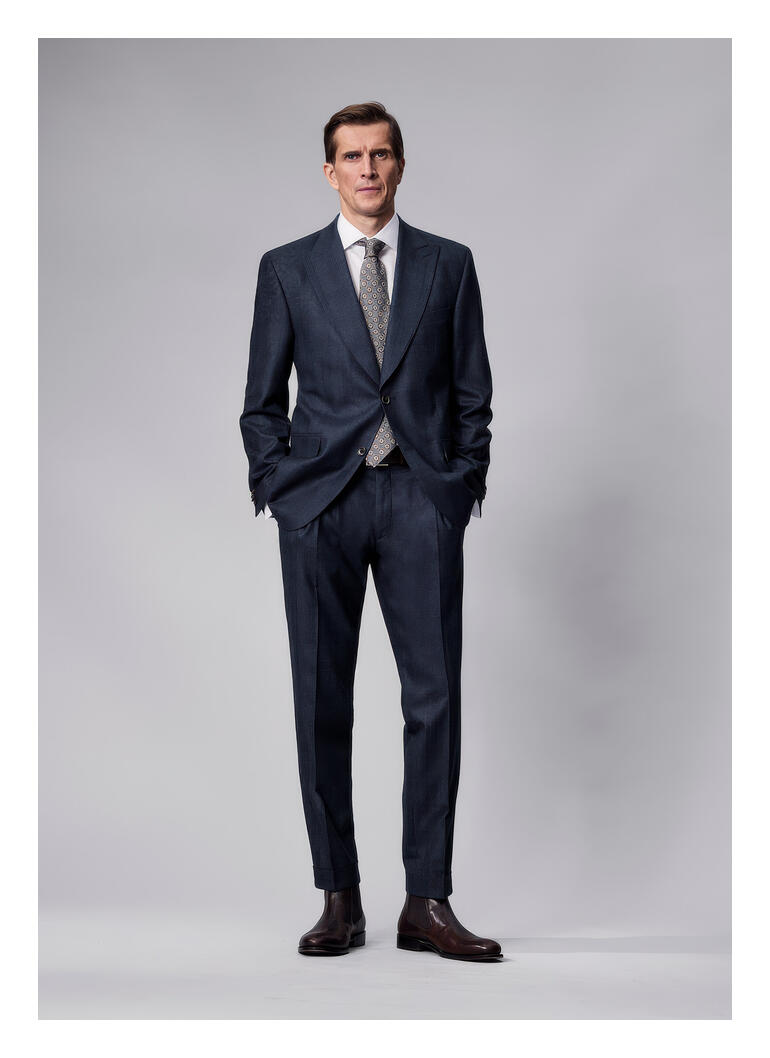 Homme en costume anthracite se tient devant un fond neutre.