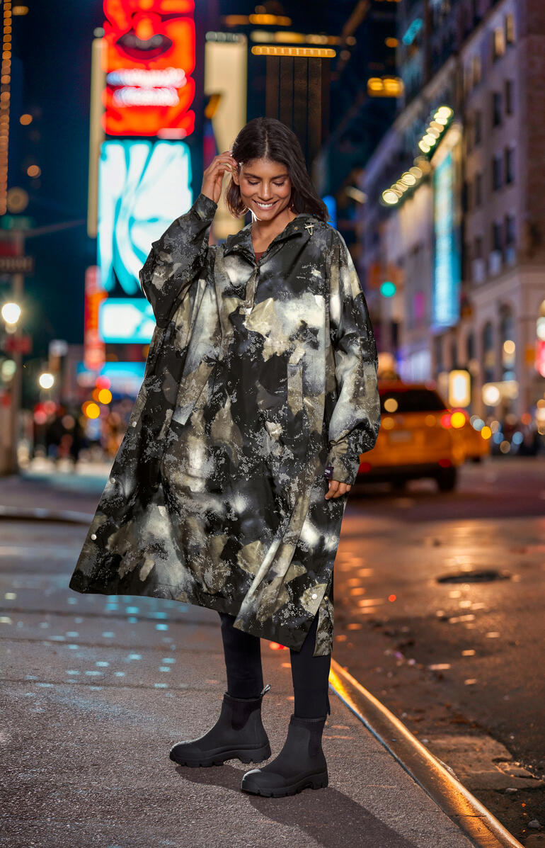 Poncho de pluie design Ilse Jacobsen Femme portant un poncho de pluie à motifs dans une ville la nuit.