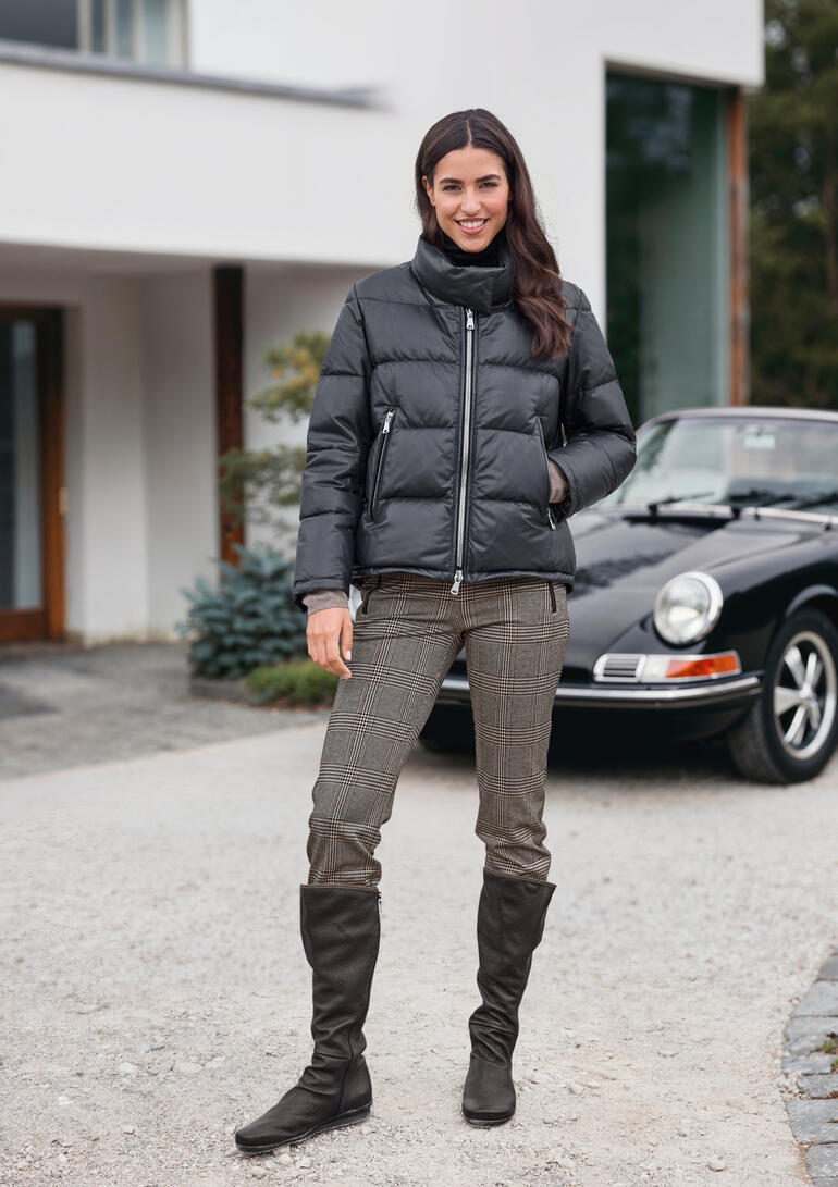 Femme en doudoune noire se tenant devant une voiture sur un chemin.