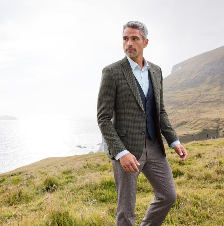Homme en blazer à carreaux dans un paysage vallonné.