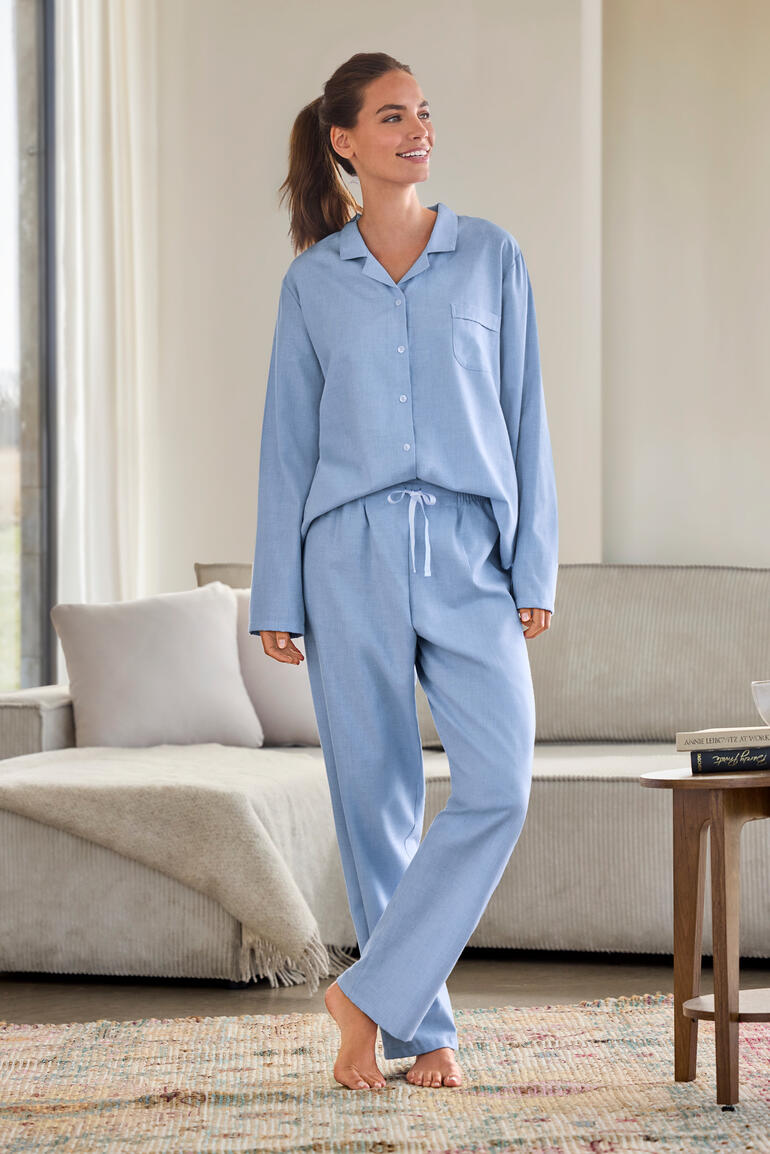 Femme portant un pyjama en flanelle de laine bleue, debout dans le salon dans une pose décontractée.
