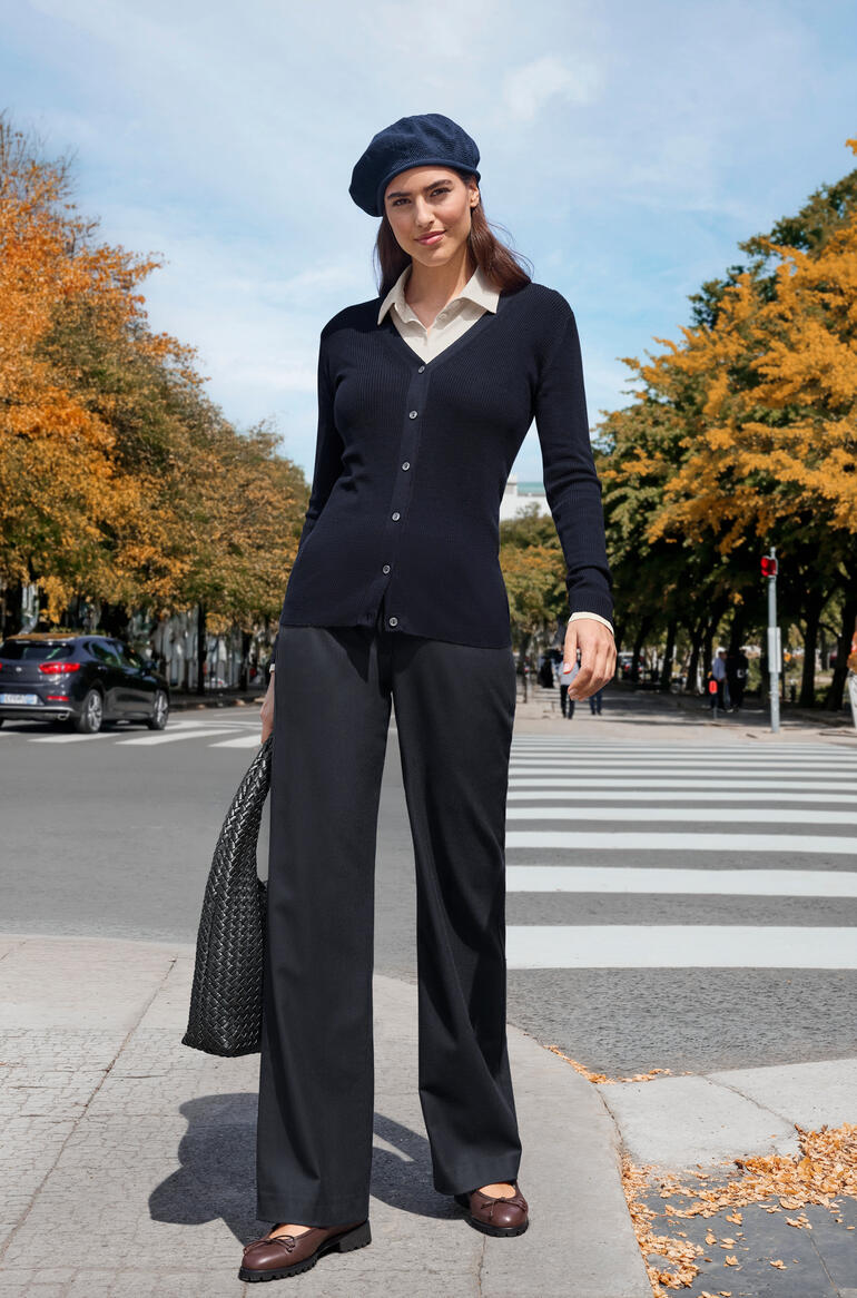Femme en cardigan bleu marine et pantalon noir dans un environnement automnal.