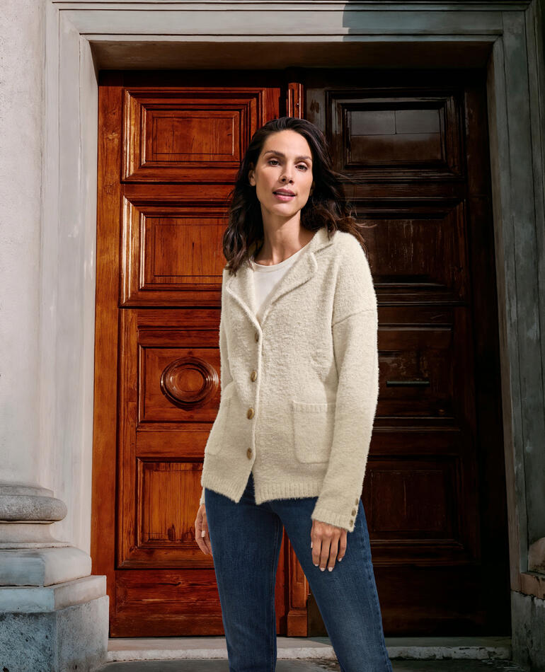 Femme en blazer tricot écru se tenant devant une porte historique.