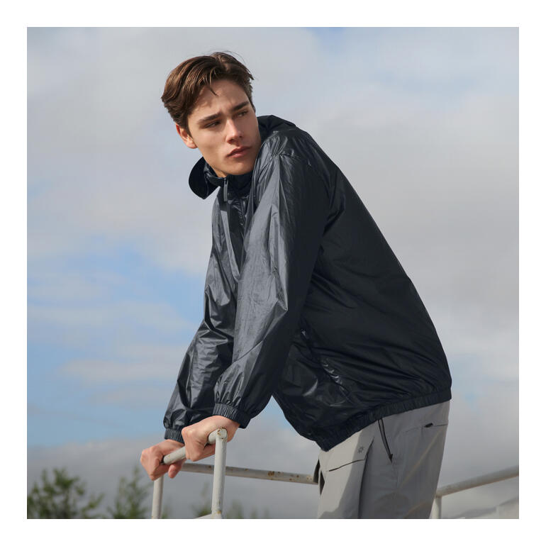 Jeune homme portant une veste de pluie noire, debout sur une plateforme.