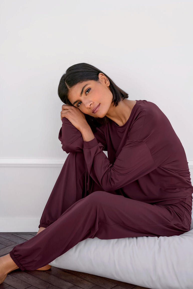 Femme assise sur un coussin portant un haut et un pantalon de loungewear mauve.
