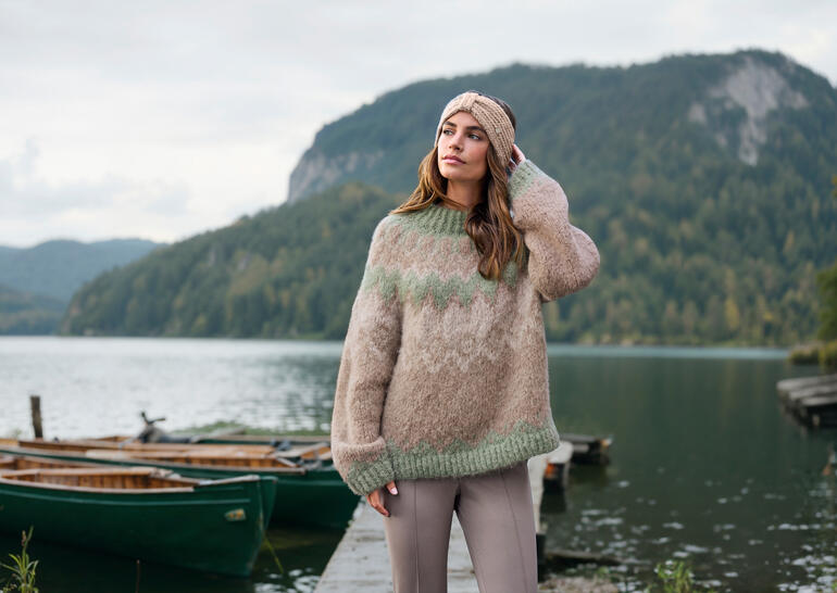Pull norvégien Granny Baestmor en teintes naturelles, porté à l'extérieur devant un décor pittoresque.