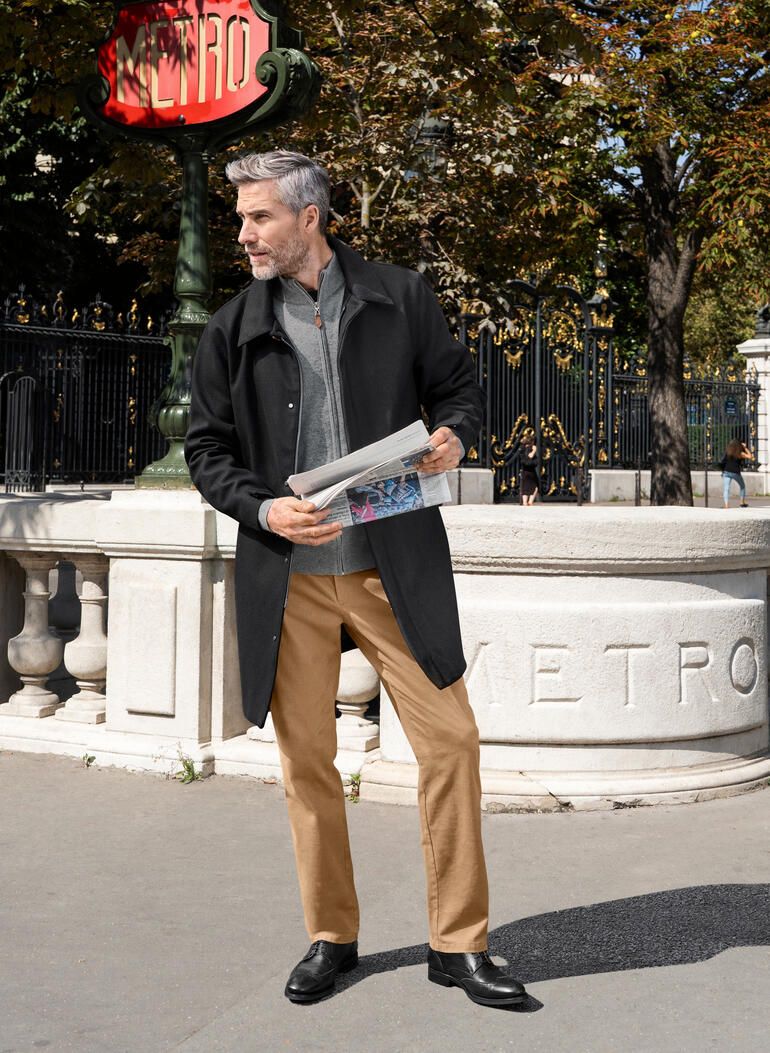 Homme en manteau en laine, se tenant devant un panneau de métro à Paris.