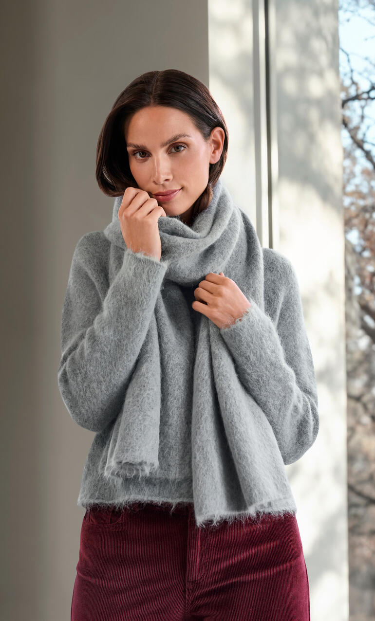 Femme avec un pull en alpaga brossé gris enroulé dans une écharpe.