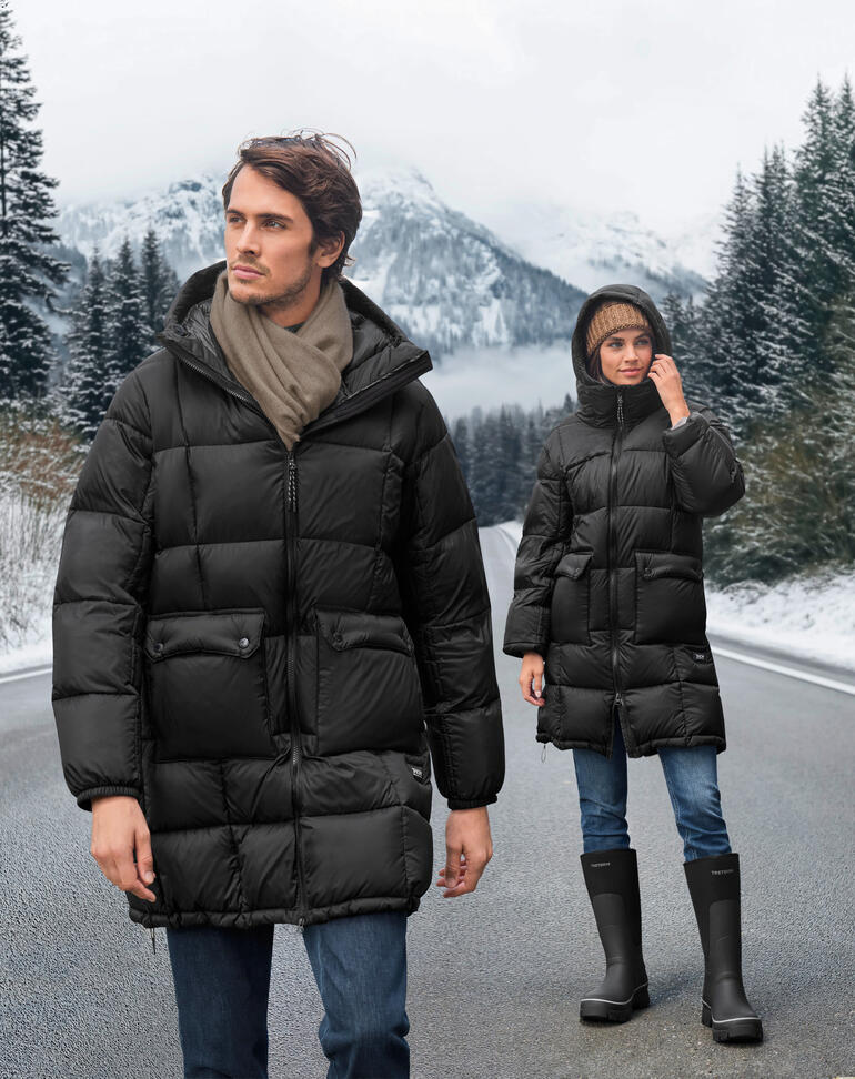 Deux personnes en parka en duvet noir sur une route hivernale avec des montagnes en arrière-plan.